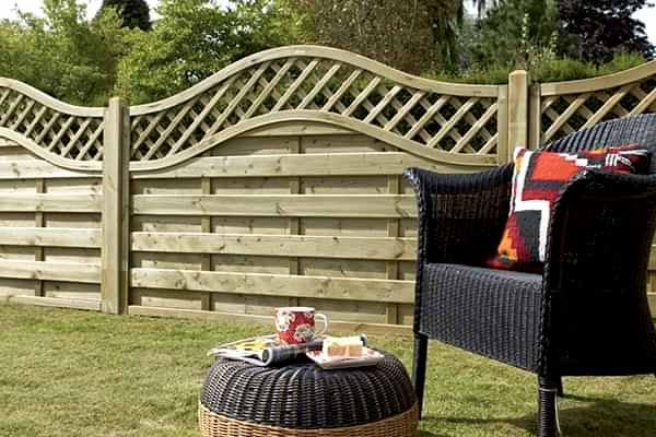 a low wooden hit and miss fence with a curved trellis top behind a garden chair and stool
