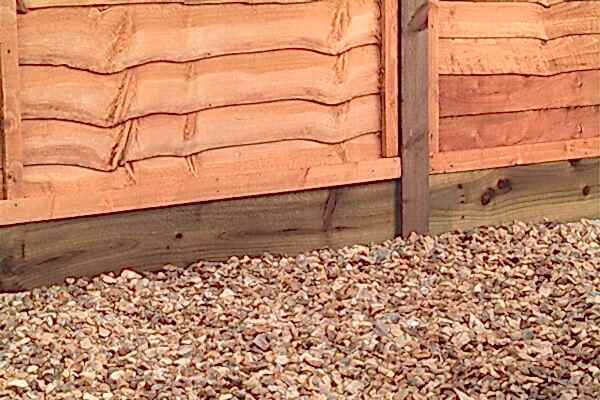a close up of a wooden gravel board under an overlap fence and sitting on a bed of gravel