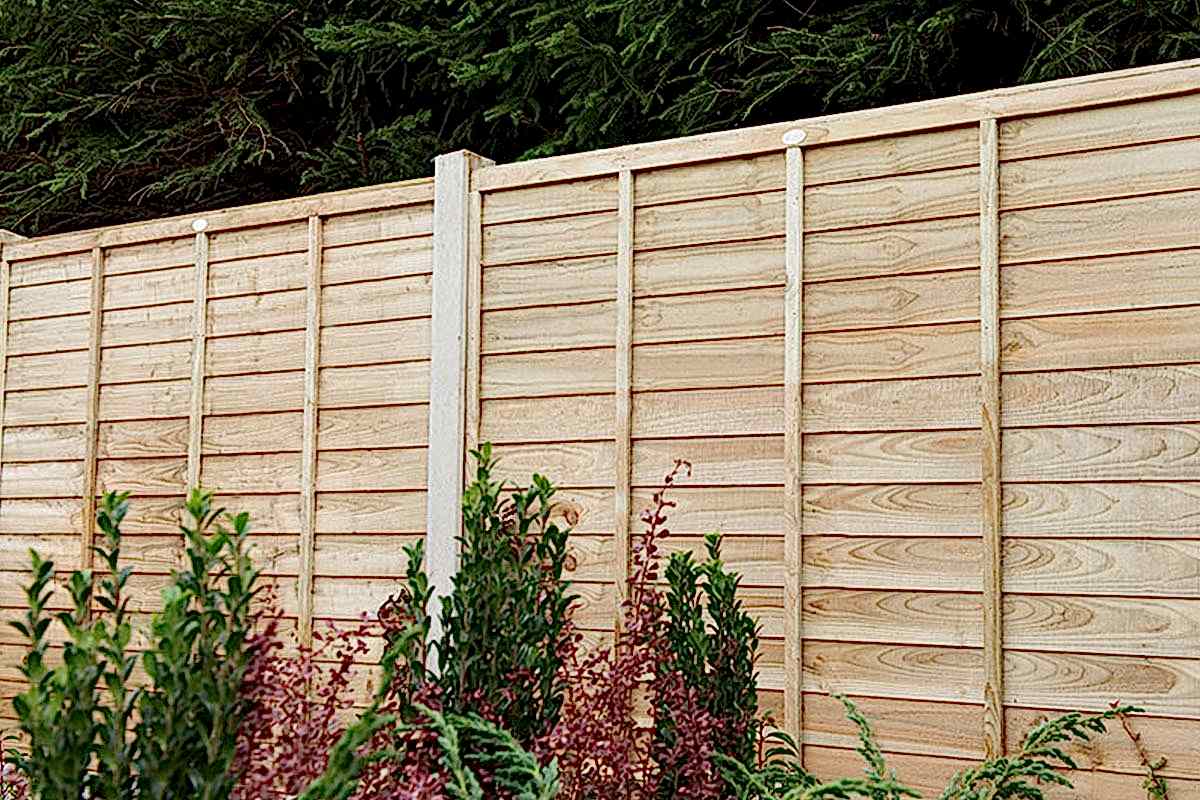 A fence run with Forest 6' x 6' Pressure Treated Lap Fence Panels and plants in front