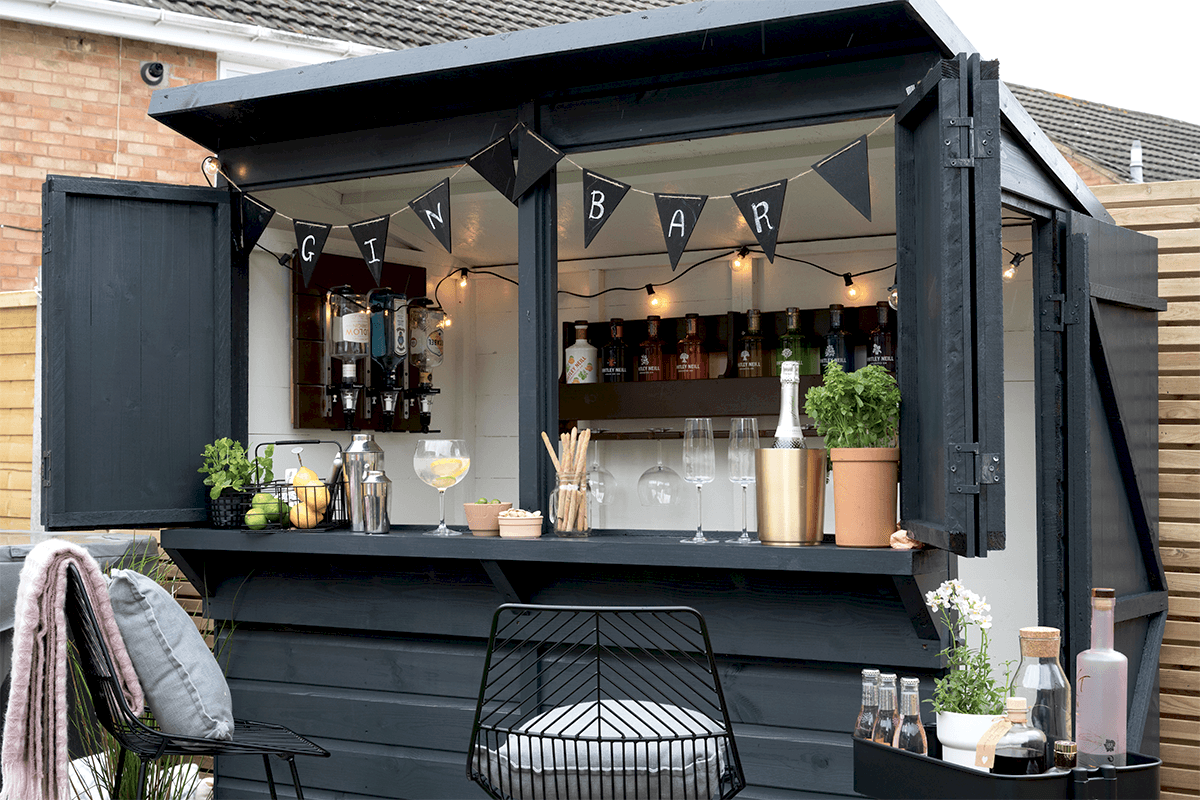 A Forest Shiplap Pressure Treated Garden Bar, painted dark grey and decorated with drinks, glasses and other bar items