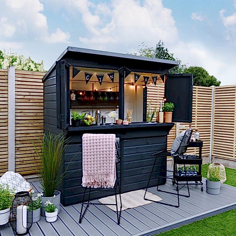 The Forest Shiplap Pressure Treated Garden Bar, painted dark blue, on decking and in front of a wooden fence