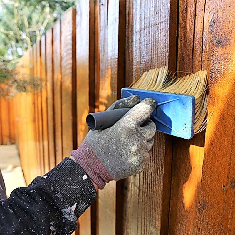 a person is brushing a fence with the best wood preserver for fence posts
