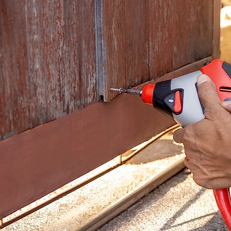 a close-up photo of someone fixing a fence by screwing a loose board back in