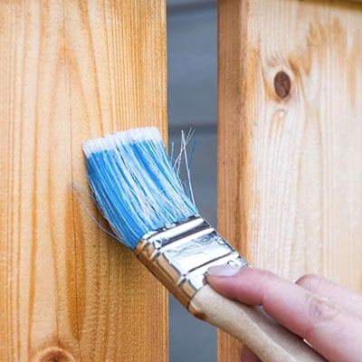 a person's hand painting a wooden fence with a blue brush